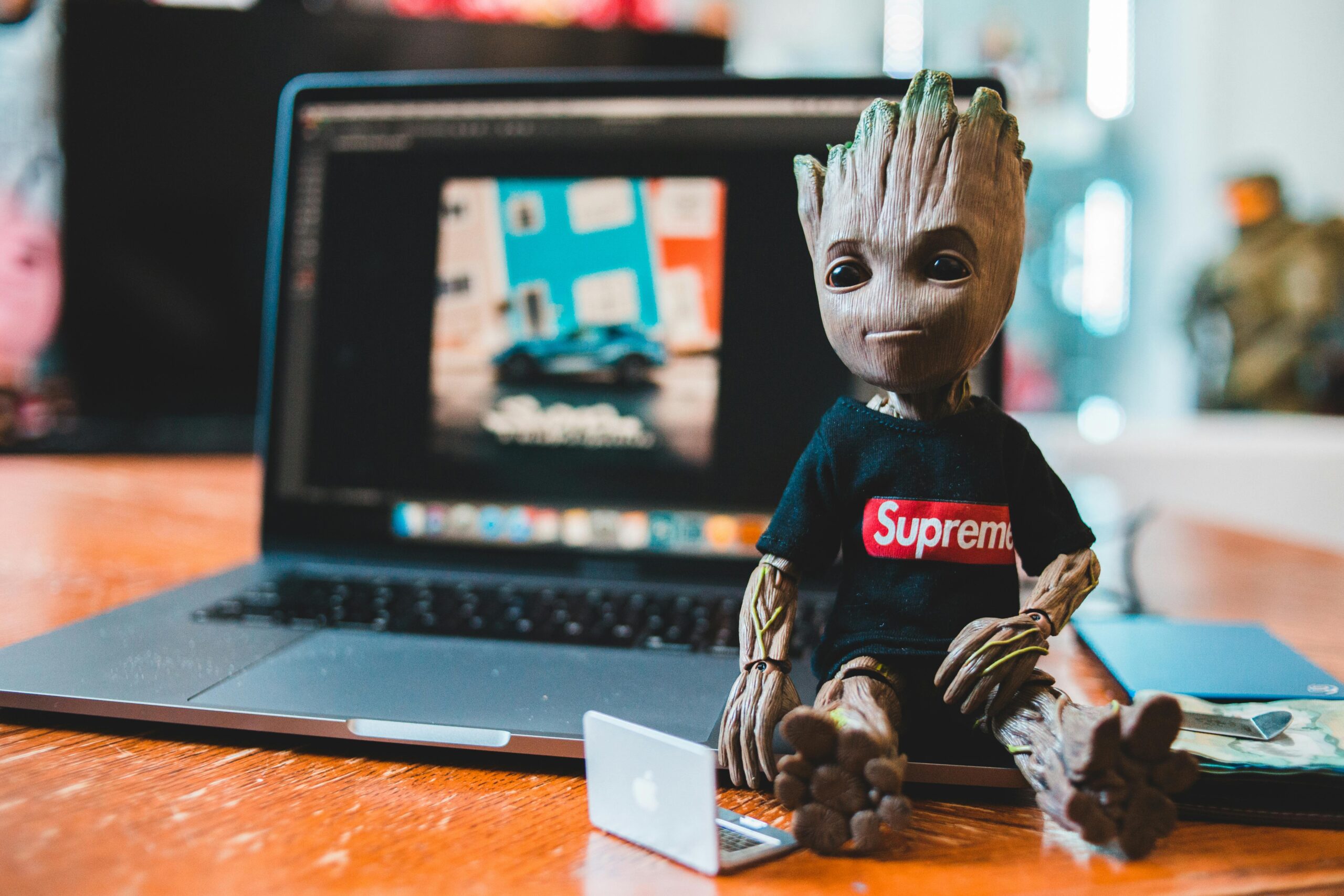 Configuração criativa com um brinquedo Groot ao lado de um laptop, mostrando um ambiente moderno de trabalho em casa.